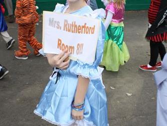 Student holding a piece of paper that reads Mrs. Rutherford Room 8